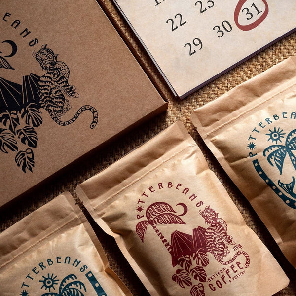 Three Potterbeans coffee bags arranged beside a monthly calendar and illustrated notebook, representing a three month coffee subscription gift