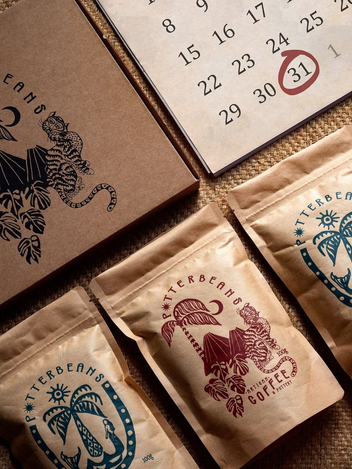 Three Potterbeans coffee bags arranged beside a monthly calendar and illustrated notebook, representing a three month coffee subscription gift